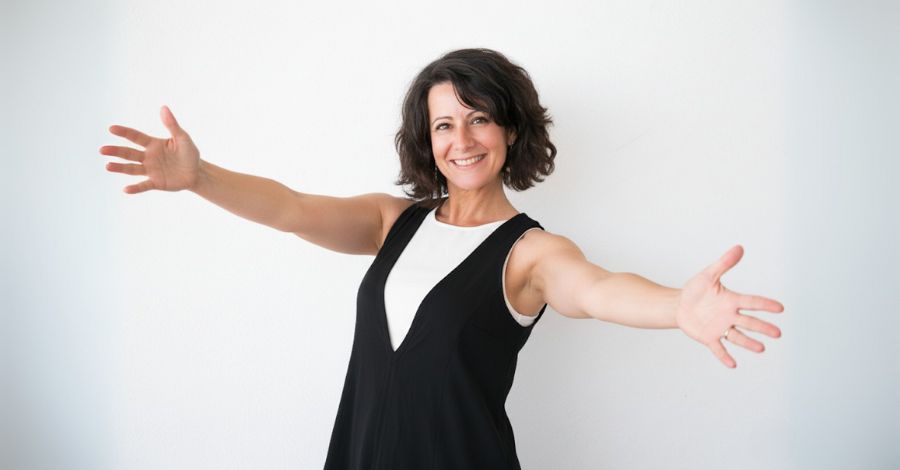 Mulher sorridente de braços abertos, expressando a autoconfiança e a autoaceitação necessárias para ter a coragem de começar.